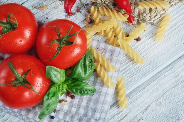 Cucina italiana con pomodori, basilico, pasta, olio d'oliva, pepe in grani, peperoncino e timo. Concetto di cibo.