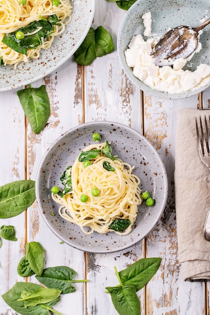 Cucina italiana: Pasta fresca all'uovo vegetariana tagliatelle fatte in casa Carbonara servita con ricotta e spinaci su sfondo bianco in legno