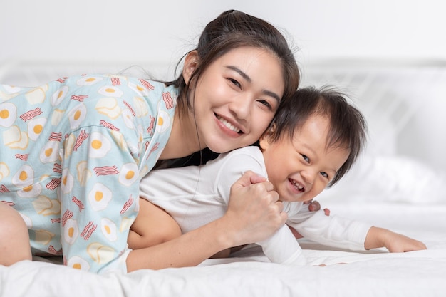 Cucina madre asiatica abbraccia il suo bambino sul letto sorriso e felicità insieme piccolo bambino si siede sul letto e si rilassa con la madre trascorrere il tempo per l'apprendimento e la crescita Buoni momenti di tempo in famiglia Giorno della Madre