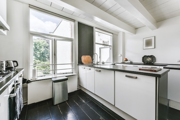Cucina moderna arredata con pavimento nero e armadi bianchi in casa con soffitti con travi a vista bianche e grandi finestre