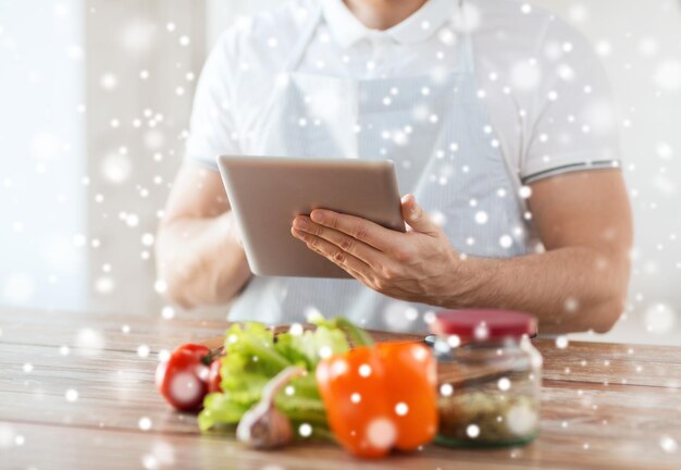 cucina, persone, tecnologia e concetto di casa - primo piano dell'uomo che legge la ricetta dal computer tablet pc e verdure sul tavolo in cucina