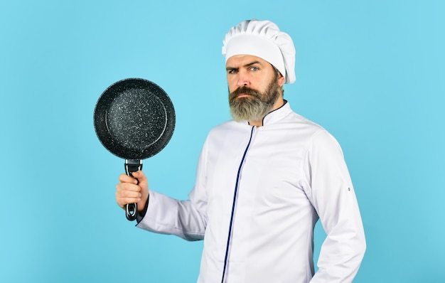 Cucina ricca di vitamine che preparano il cibo in cucina marito in cappello da chef in cucina Concetto di cibo da cucina Tenere la padella della migliore qualità cuoco barbuto in uniforme con strumenti uomo barbuto tenere la padella