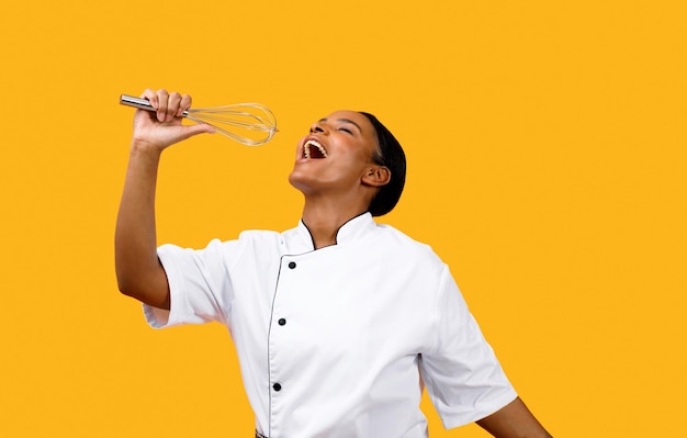Cucinare divertente chef nero donna in uniforme che canta con la frusta in mano