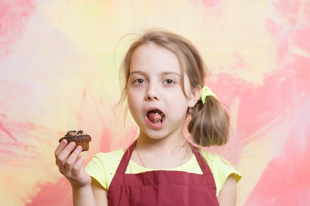 Cucinare e mangiare. Bambino dello chef con cupcake. Bambino in grembiule da cuoco. Infanzia ed educazione. Piccola ragazza su sfondo colorato.