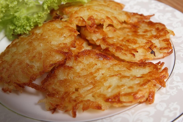 Cucinare frittelle di patate fatte in casa con insalata verde su un piatto bianco su sfondo di legno Concetto di cibo vegetariano Primo piano