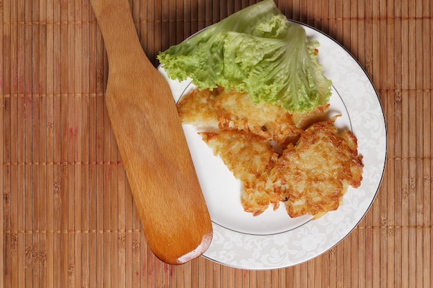 Cucinare frittelle di patate fatte in casa con insalata verde su un piatto bianco su sfondo di legno Concetto di cibo vegetariano Primo piano