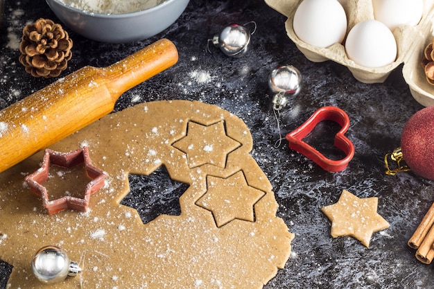 Cucinare i biscotti di panpepato di Natale con ingredienti e decorazioni su uno sfondo scuro