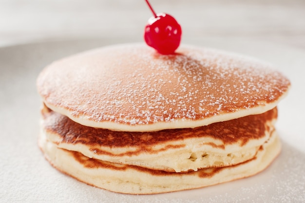 Cucinare il cibo. Pancake americani con la ciliegia sul fondo bianco del piatto. Pasto tradizionale degli Stati Uniti.