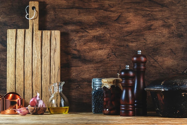 Cucinare il cibo sfondo rustico tavolo da cucina in legno padella in ghisa macinini per spezie tagliere spezie e condimenti vasetti di stoccaggio Copia spazio