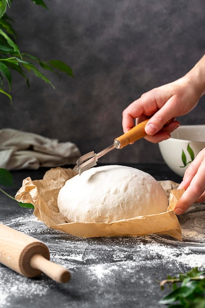 Cucinare il pane a lievitazione naturale in casa. Mano femminile che taglia la pasta di pane appena lievitata con una zoppa, preparandosi per la cottura.