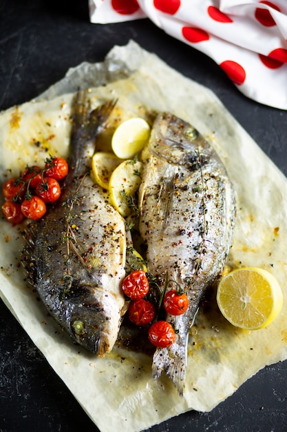 Cucinare il pesce in forno. Dorado di cottura con pomodorini ed erbe su pergamena nel forno.