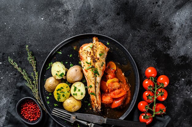 Cucinare in pomodori rana pescatrice con patate al forno. Pesce fresco. Sfondo nero