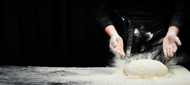 Cucinare l'impasto dalle mani dello chef per il pane di pasticceria fatto in casa con spruzzi di farina su uno sfondo scuro