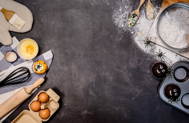 Cucinare la torta di Halloween festiva a casa. In casa cuocere gli ingredienti con farina su sfondo scuro con copia spazio per il testo.