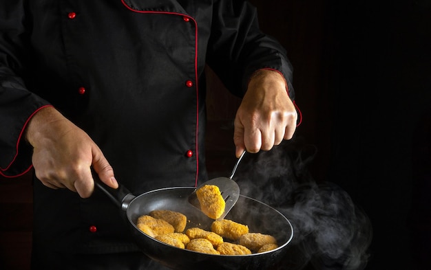 Cucinare nuggets di pollo croccanti Lo chef gira i nagits in una padella calda affumicata L'idea di una grande cucina per un hotel con uno spazio pubblicitario