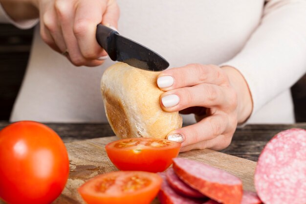 Cucinare panino ragazza non abile con panino, salsiccia e verdure, primo piano a casa