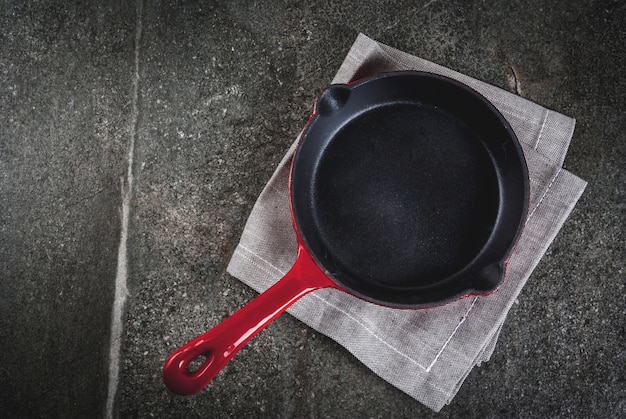 Cucinare sfondo di cibo. Padella rossa vuota del ghisa con un asciugamano su una tavola di pietra nera