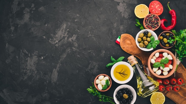 Cucinare un'insalata caprese Mozzarella pomodorini olive basilico foglie olio pepe Su un tavolo di pietra nera Spazio libero per il testo