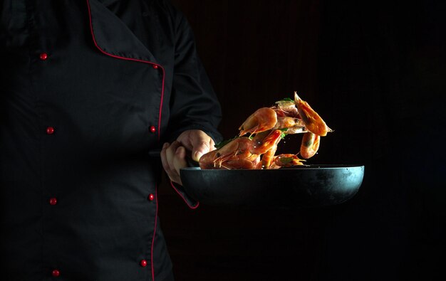 Cucino di gamberi nella cucina del ristorante Volo di gamberi su una padella nella mano dello chef Spazio scuro per la ricetta o il menu