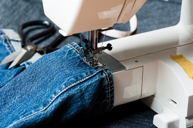 Cucire jeans denim indaco con macchina da cucire, concetto industriale di abbigliamento.