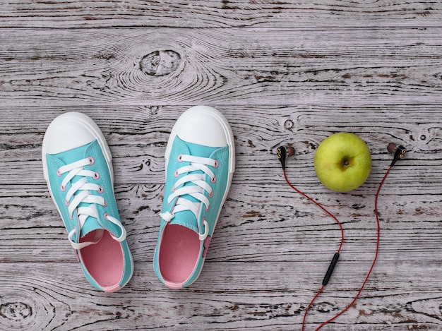 Cuffie, Apple e scarpe da ginnastica sul pavimento di legno. Stile sportivo. Lay piatto. La vista dall'alto.