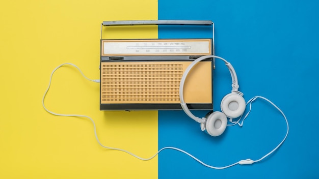 Cuffie bianche collegate a una radio antica su sfondo giallo e blu Tecnica vintage