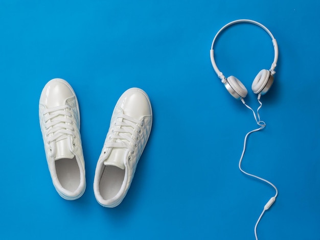 Cuffie bianche e scarpe da ginnastica bianche su sfondo blu. Il concetto di uno stile di vita sano e musica.