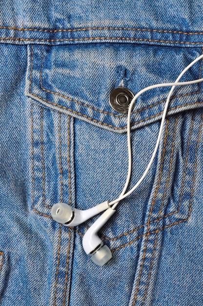 Cuffie bianche per il telefono sulla superficie di una giacca di jeans. avvicinamento.