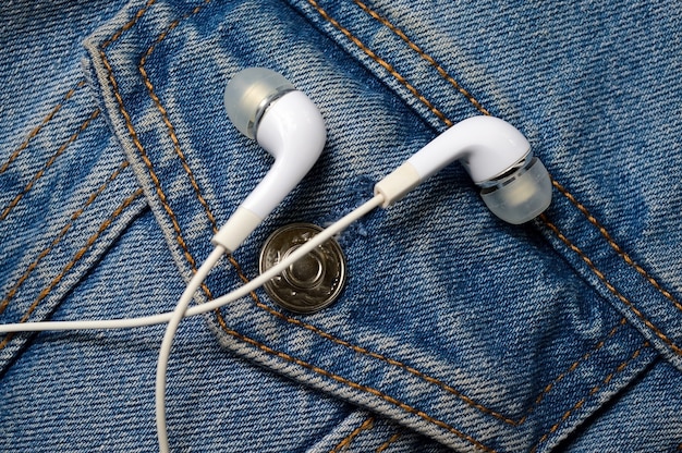 Cuffie bianche per il telefono sullo sfondo di una giacca di jeans. avvicinamento.