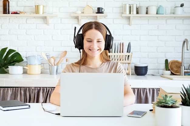 Cuffie d'uso dell'adolescente femminile che studiano al computer portatile a casa