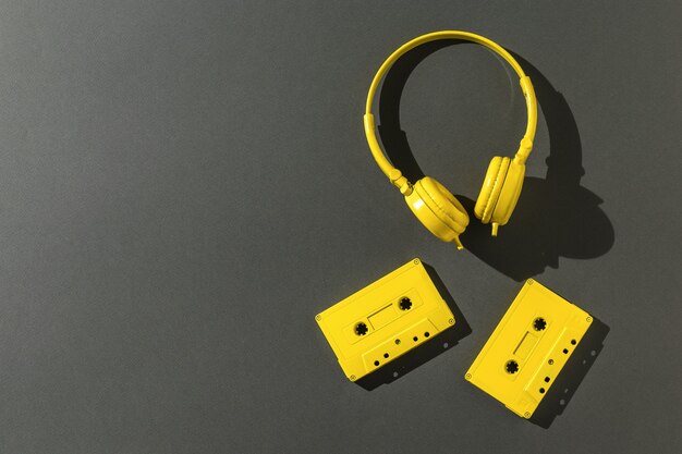 Cuffie gialle e due cassette a nastro in condizioni di luce intensa su sfondo nero. Spazio per il testo. Tendenza colore. Disposizione piatta.