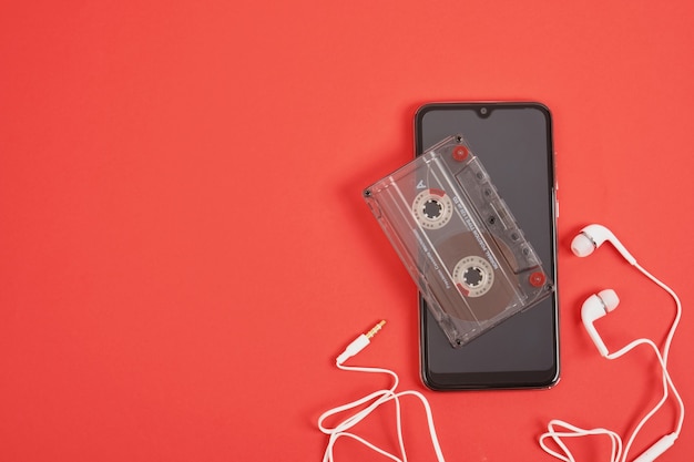 Cuffie per smartphone e audiocassetta su sfondo rosso, concetto di memorie, tecnologie moderne e tecnologie del passato