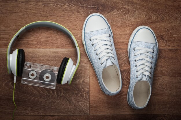 Cuffie stereo, cassetta audio e scarpe da ginnastica su un pavimento di legno. Media retrò