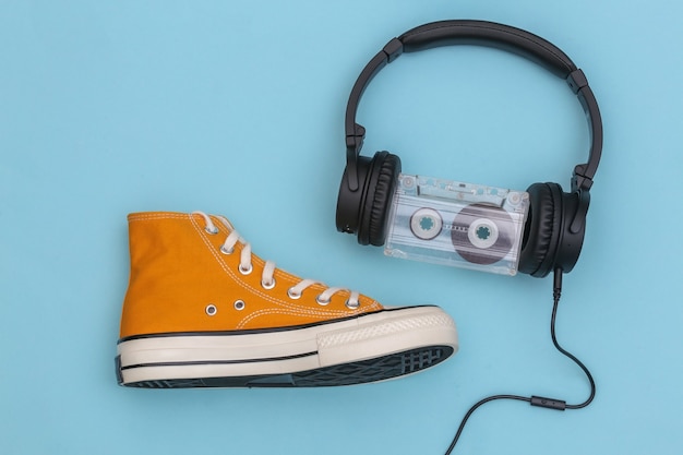 Cuffie stereo con audiocassetta e sneaker retrò su sfondo blu pastello. Vista dall'alto. Lay piatto