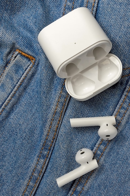 Cuffie stereo wireless bianche con custodia si trovano sul denim.