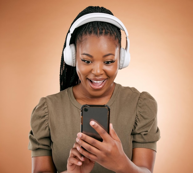 Cuffie telefono e sorpresa donna nera isolata su sfondo studio per promozione vendita musica o sconto annuncio Wow o notizie su smartphone persona africana o vincitore ascolto audio