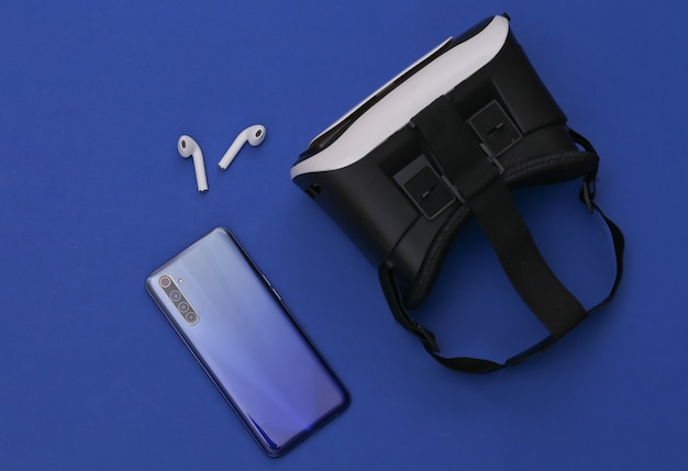 Cuffie VR, smartphone e cuffie wireless su sfondo blu classico.