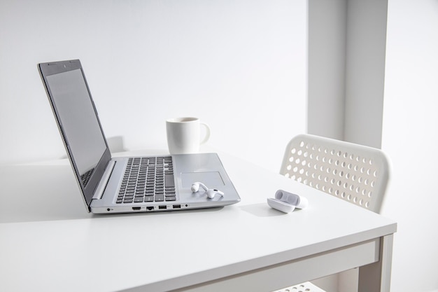 Cuffie wireless con tazza per laptop su un tavolo bianco Ambiente di lavoro per liberi professionisti