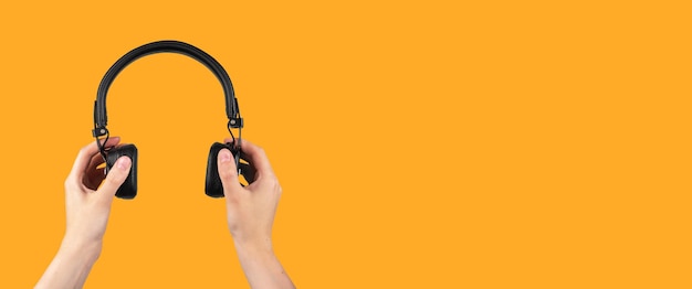 Cuffie wireless nere in mano su banner di sottofondo musicale arancione