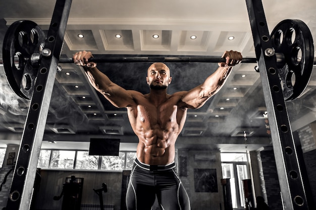 Culturista calvo che prepara per l'esercizio con il bilanciere in palestra