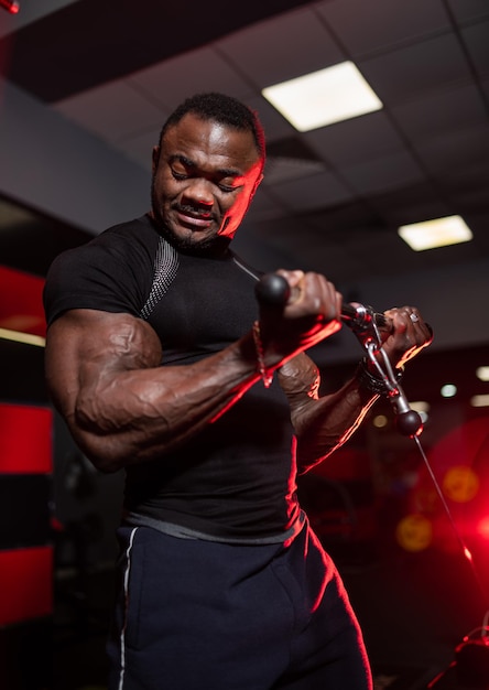 Culturista maschio in abbigliamento sportivo scuro che fa allenamento per le mani in palestra moderna. Atleta bello con un corpo forte e perfetto.