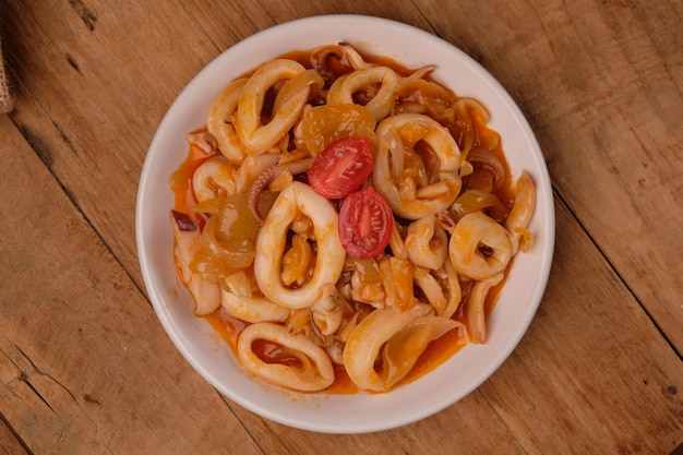 Cumi-cumi asam manis o calamari in agrodolce. servito su un piatto quadrato di ceramica. pomodori, cipolle.