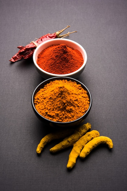 Cumulo di curcuma o haldi e peperoncino rosso o polvere di mirchi in una ciotola di ceramica su una superficie bianca o nera