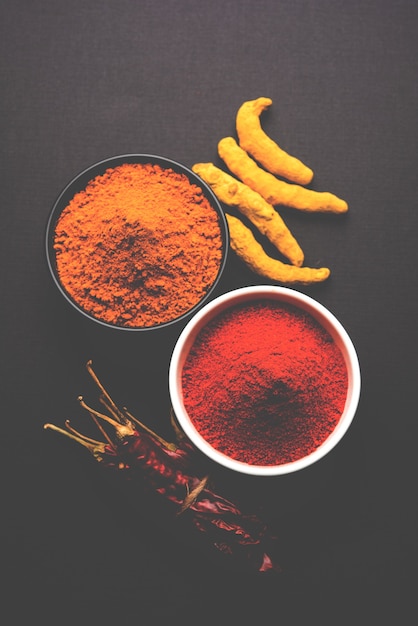 Cumulo di curcuma o haldi e peperoncino rosso o polvere di mirchi in una ciotola di ceramica su una superficie bianca o nera