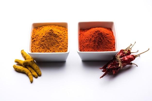 Cumulo di curcuma o haldi e peperoncino rosso o polvere di mirchi in una ciotola di ceramica su una superficie bianca o nera