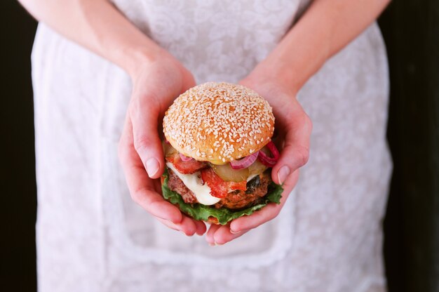 Cuoca donna che tiene in mano un delizioso e succoso hamburger fatto in casa in stile rustico con una grossa braciola di manzo