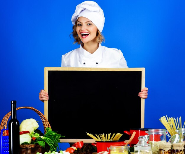 Cuoca sorridente con un menu sano per la preparazione del cibo sulla lavagna vuota in uniforme da chef con