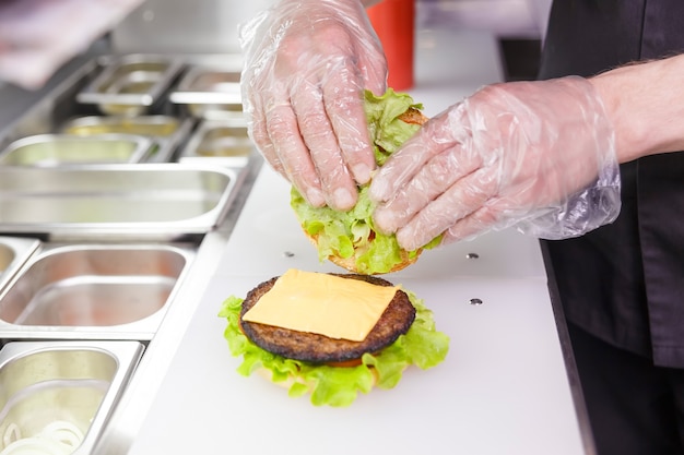 Cuocere aggiungendo una seconda metà dell'hamburger. Preparare hamburger nel ristorante. Mani del cuoco in guanti usa e getta in base ai requisiti di igiene.