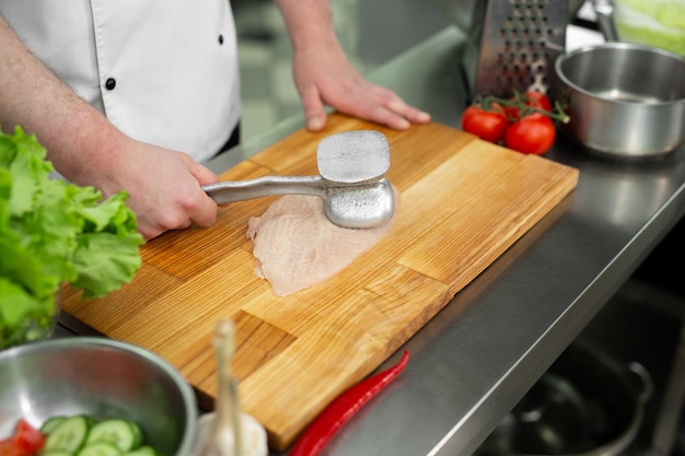 Cuocere battendo un petto di pollo con un martello, primo piano. Dieta, cibo sano a basso contenuto calorico, concetto di perdita di peso