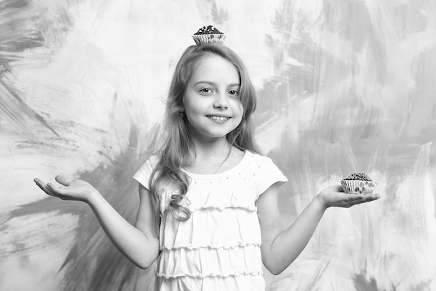 Cuocere il bambino o la ragazza felice con il cupcake in testa e in mano il bambino ha i capelli lunghi e la faccia sorridente su sfondo colorato che cucina e mangia cibo e dessert